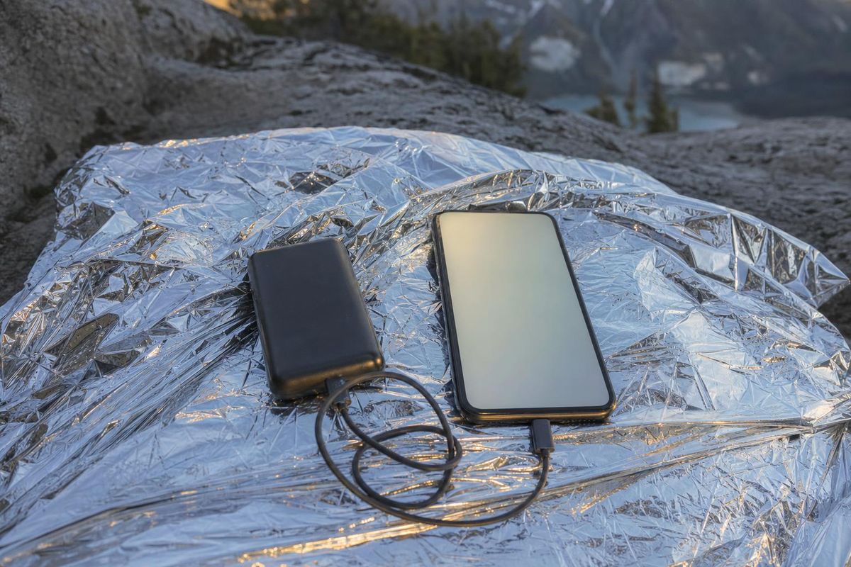 Powerbank und Kabel neben einem Handy auf einer Rettungsdecke, Abendlicht in den Bergen