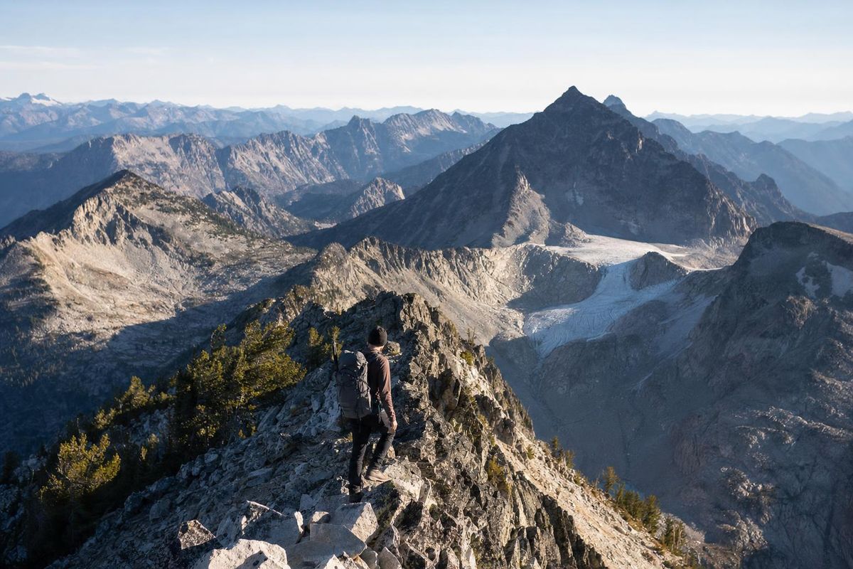 Wanderin auf einem Grat in unbekanntem Gelände, weite Sicht über mehrere Ketten