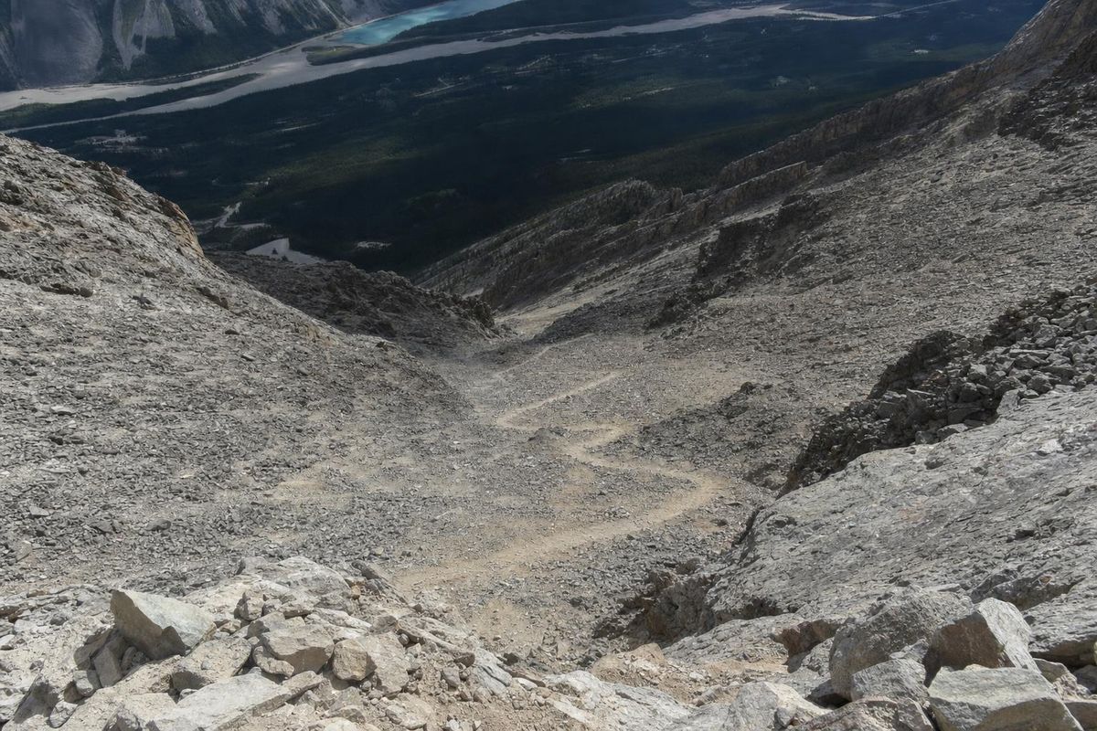 Steiler Geröllabstieg von oben gesehen, ein schmaler Pfad zieht sich in Serpentinen ins Tal