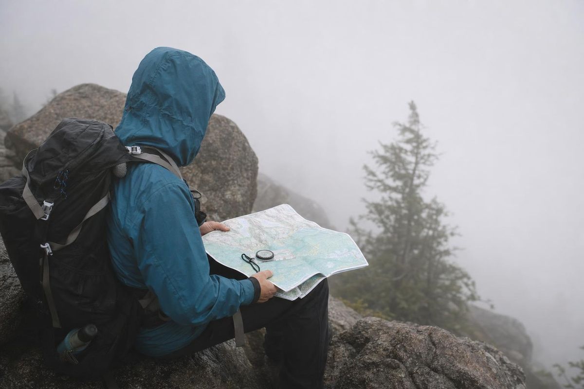 Wanderin bestimmt im Nebel ihre Position mit Karte und Kompass, sitzend auf einem Fels