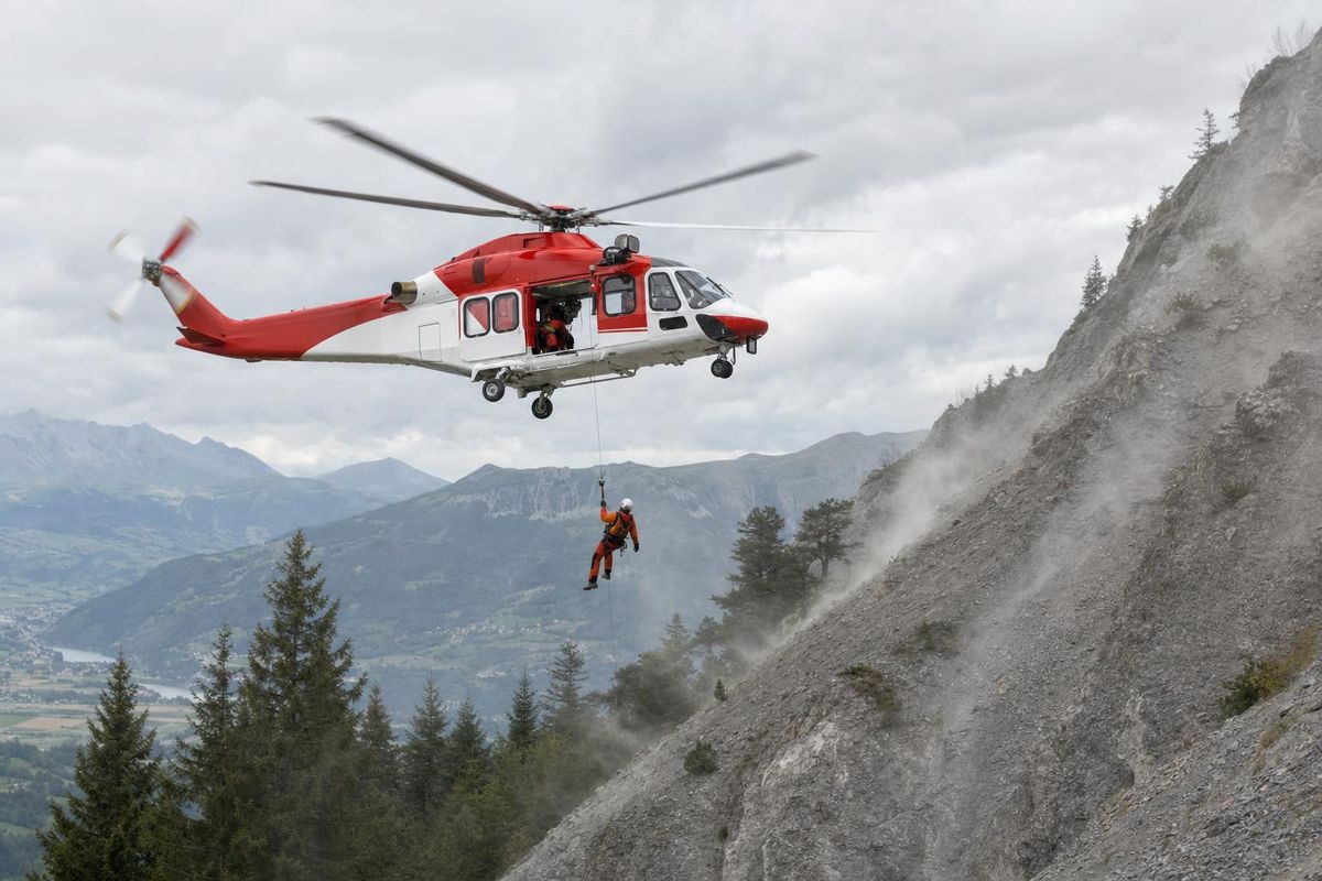 Rettungshubschrauber im Schwebeflug über einem felsigen Steilhang, ein Retter an der Winde