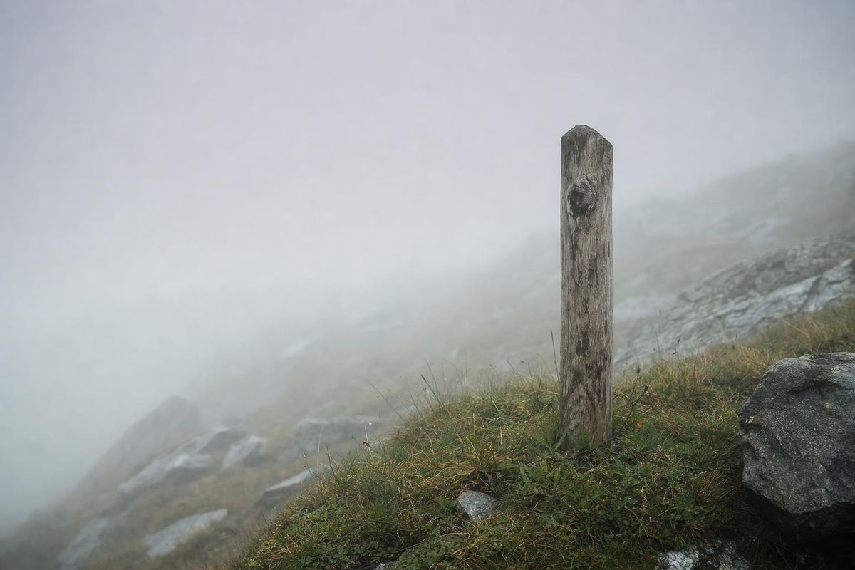 Dichter Nebel auf einem Bergrücken, ein Wegweiserpfosten verschwindet nach wenigen Metern im Grau