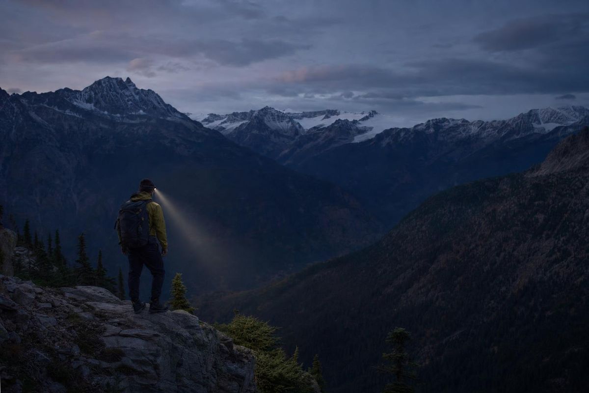 Wanderer signalisiert in der Dämmerung mit einer Stirnlampe von einem Felsvorsprung ins Tal