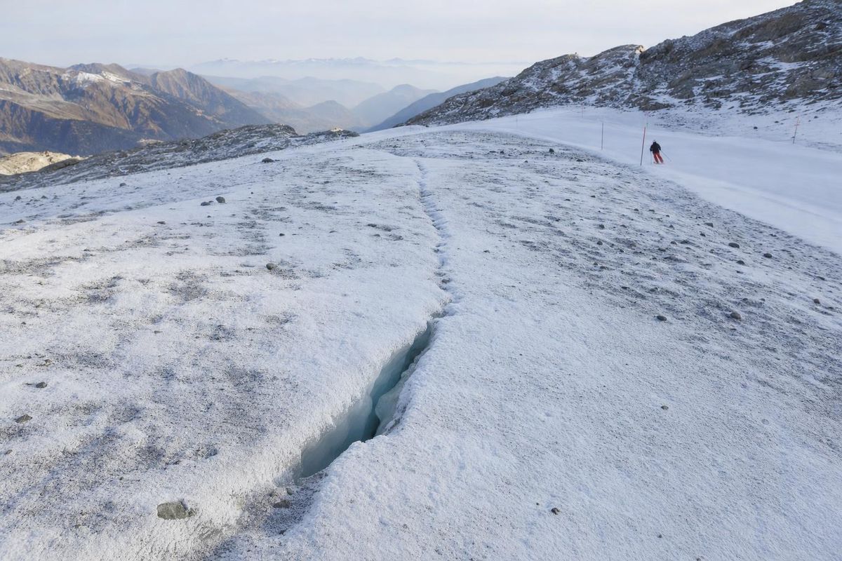 Gletscher neben einer markierten Piste, dünner Neuschnee überdeckt eine schmale Spalte, im Hintergrund Pistenstangen