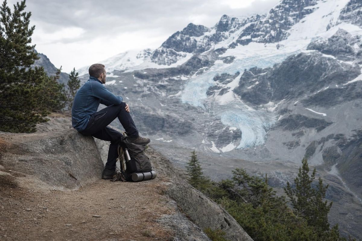 Wanderin sitzt am Wegrand, das Bein hochgelegt, Rucksack als Unterlage